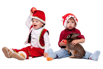 Two kids in Santa hats with a rabbit