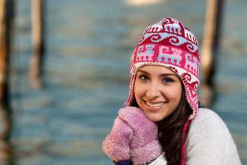 Pretty young woman in winter clothing along the bay at sunset