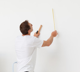 Handsome man looking at a wall with ruler and tools
