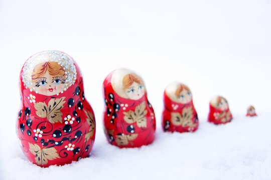 Russian dolls in varies sizes displayed across white snow in a straight line 