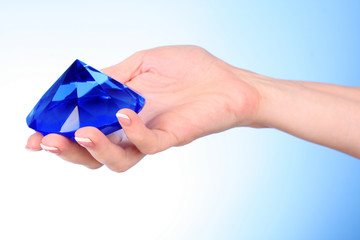 Woman hand with big blue crystal on blue background