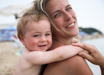 Little boy and his pretty mother play together at beach