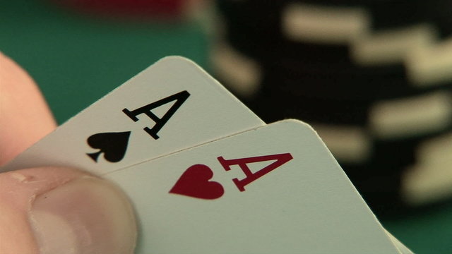 Hand holding pocket aces with poker chips