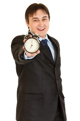 Smiling young businessman holding alarm clock in hand