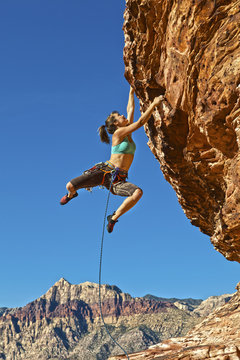 Female rock climber clinging to a cliff.