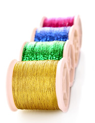 Pile of coloured bobbins of lurex thread isolated on white