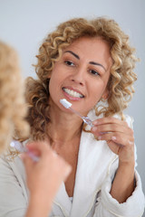 Portrait of woman brushing her teeth in front of mirror
