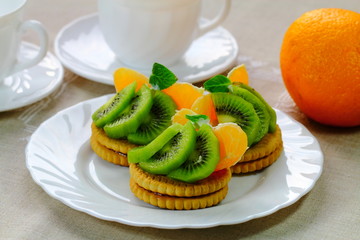 Pieces of kiwi fruit and orange with biscuits on the plate