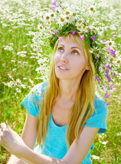 The happy young woman in a wreath from wild flowers in the field
