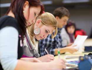 pretty female college student sitting in a classroom full of stu