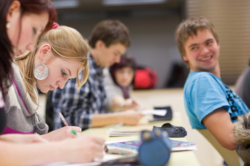 pretty female college student sitting in a classroom full of stu
