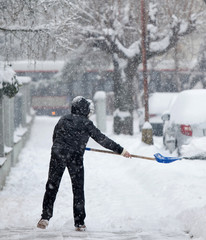 Naklejka premium Woman shoveling snow from a sidewalk after a heavy snowfall in a