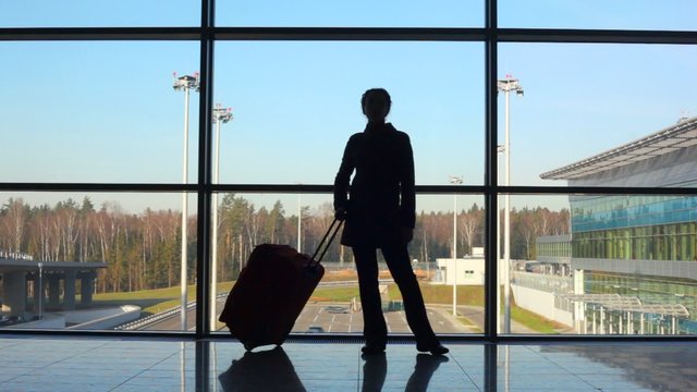 silhouette of woman with travel luggage stands against window