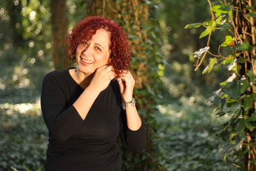 Red hair woman standing outdoors in a beautiful green forest