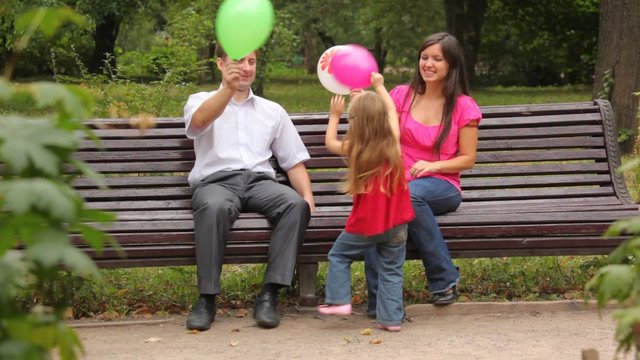 family throws balloons sitting on bench in park