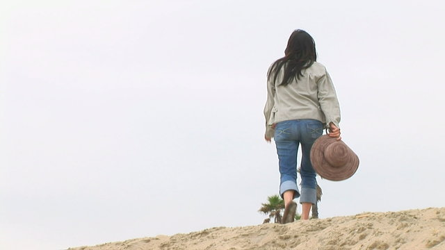 Young woman walking on sand dunes at beach in cool weather