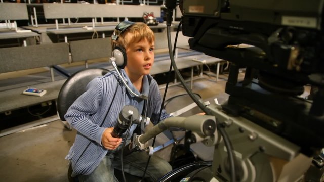 boy operating stationary camera in big TV studio with spectators