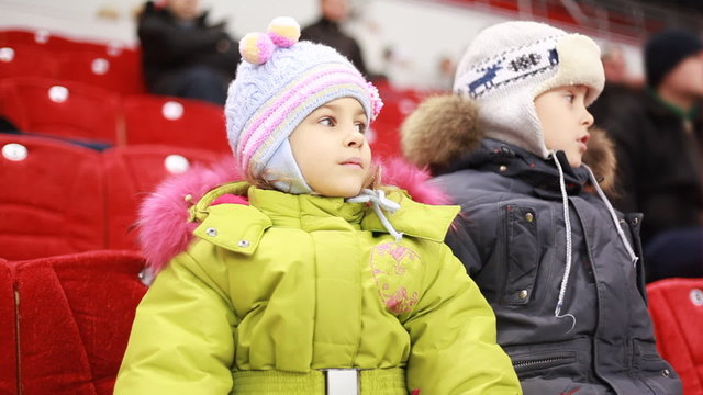 girl and boy sit on armchairs, attentively watch hockey match