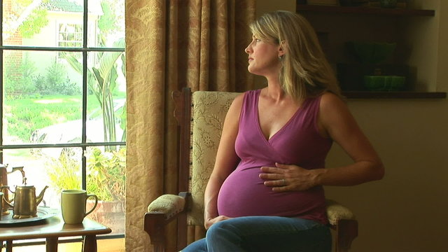 Portrait of pregnant woman by window caressing her belly