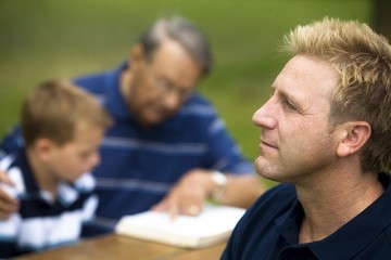 Man Reflecting While His Family Is Reading
