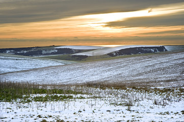 Winter snow landscape over fields with trees and glowing sunset