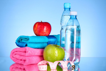 Blue bottle of water, apple, sports towel and measure tape on bl