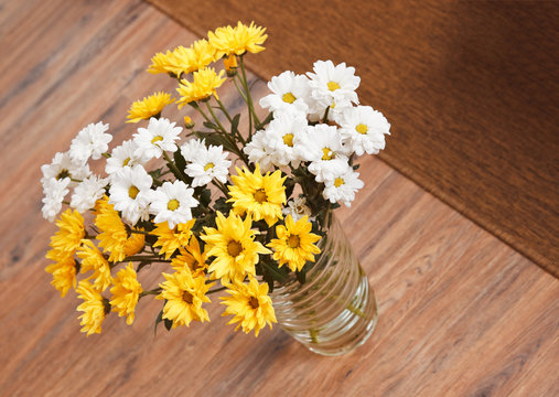 Bouquet of chamomile flowers in glass vase on wooden floor