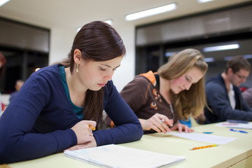 pretty female college student sitting an exam in a classroom ful