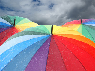 Rainbow umbrellas with snowflakes on dramatic sky background