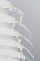 Fototapeta na wymiar Row of Icicles Hanging off a Roof Gray Sky Background