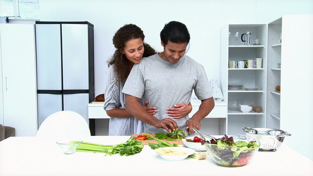 Woman eating while her husband is cooking vegetables