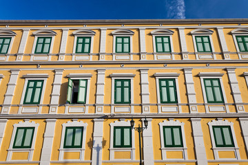 Fototapeta na wymiar yellow building with green windows beside road and sky