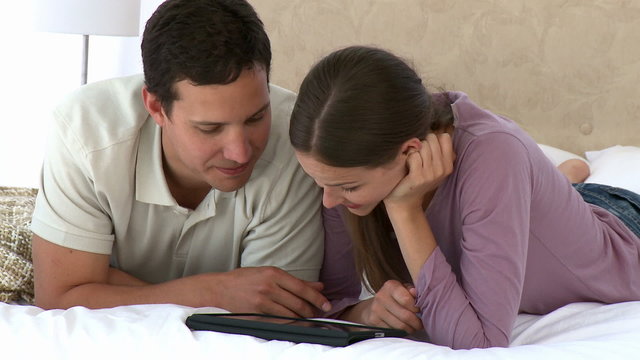 Couple using a computer tablet lying on the bed