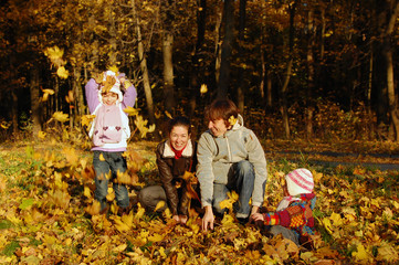 Naklejka premium Happy family with two kids throwing leaves in autumn park