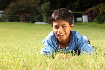 Naklejka na ściany i meble Young boy smiling lying on the grass in park