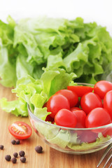 Tomatoes and lettuce in a glass bowl on a wooden chopping board
