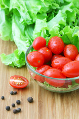 Tomatoes and lettuce in a glass bowl on a wooden chopping board