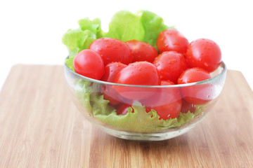 Tomatoes and lettuce in a glass bowl on a wooden chopping board