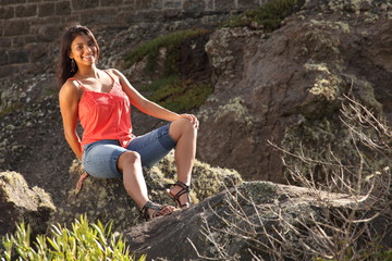 Young pretty ethnic girl sitting on rock outdoors