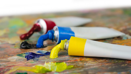 Tubes with acrylic or oil paint and brush over colorful artist's palette, selective focus