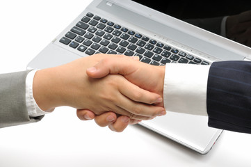Business people shaking hands over a laptop.
