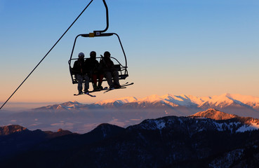 Chair ski lift with skiers over blue sky in the evening