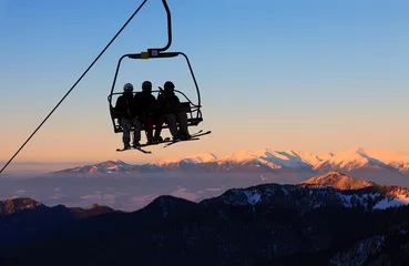Schilderijen op glas Chair ski lift with skiers over blue sky in the evening © Andrey Bandurenko