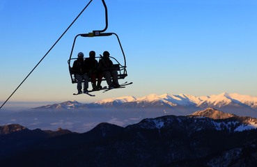 Chair ski lift with skiers over blue sky and mountains