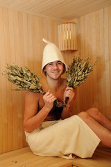 Young handsome man in a towel relaxing in a russian wooden sauna