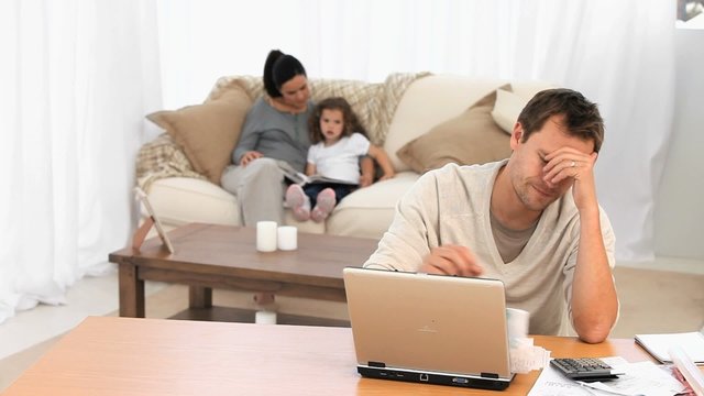 calculating bills while his wife reads a book to their daughter