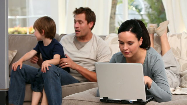 Woman using laptop with his family in the background