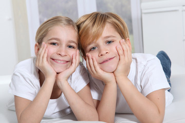 Blond children laying in sofa with hands on chin