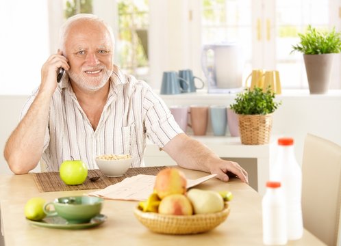 Healthy pensioner using cellphone at breakfast