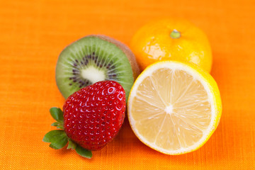 Fototapeta na wymiar kiwi,lemon,mandarin and strawberries lying on the orange fabric